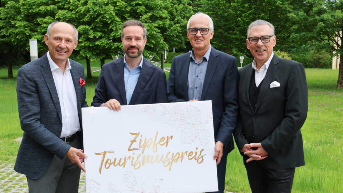 Vier Männer in Anzügen halten ein Schild mit der Aufschrift Zipfer Tourismuspreis im Freien mit grünen Bäumen im Hintergrund.