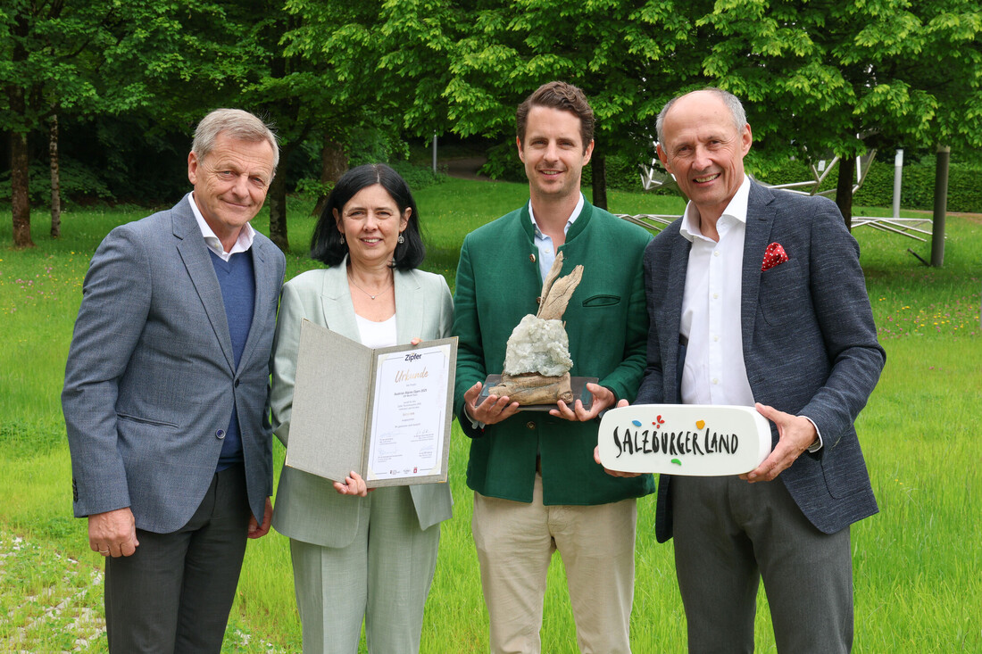 Vier Personen stehen auf einer Wiese und halten eine Urkunde, eine Trophäe und ein Schild mit der Aufschrift SalzburgerLand.