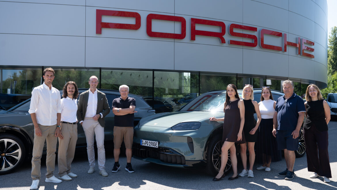 Eine Gruppe von Menschen, die an einem sonnigen Tag vor einem Porsche-Autohaus und einem Porsche-Sportwagen stehen.