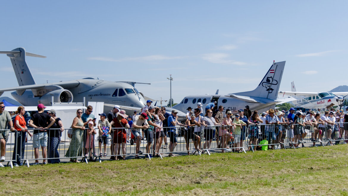 Eine Menschenmenge, die an einem sonnigen Tag bei einer Flugshow im Freien Flugzeuge beobachtet, im Hintergrund stehen Jets.