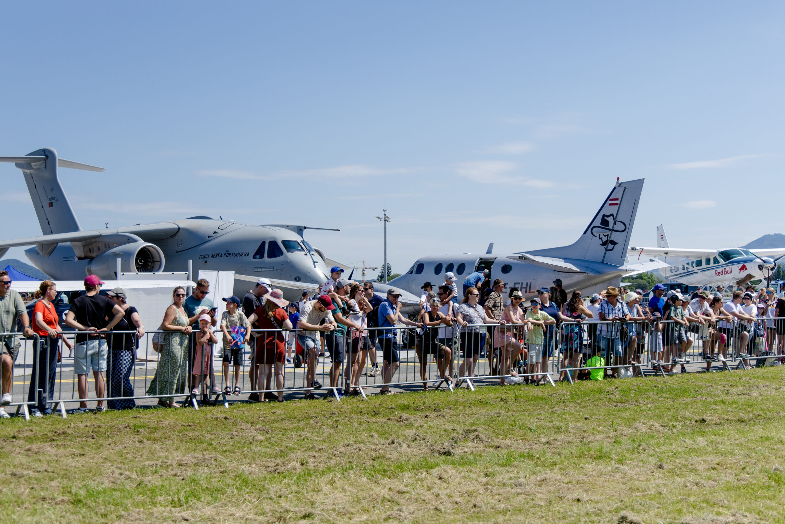 Eine Menschenmenge, die an einem sonnigen Tag bei einer Flugshow im Freien Flugzeuge beobachtet, im Hintergrund stehen Jets.