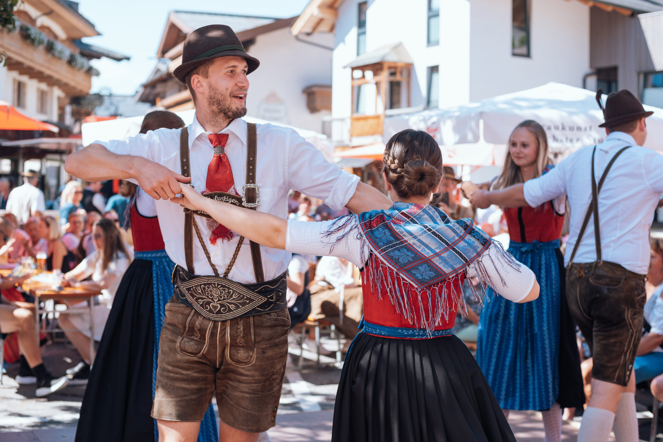 Menschen in traditioneller österreichischer Tracht führen bei einem Volksfest im Freien vor Zuschauern einen Volkstanz auf.