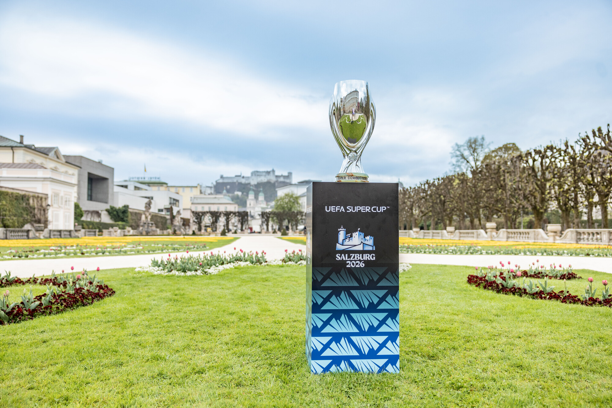Die Trophäe des UEFA-Supercups auf einem Sockel in einem Garten, auf dem Sockel steht „Salzburg 2026“.