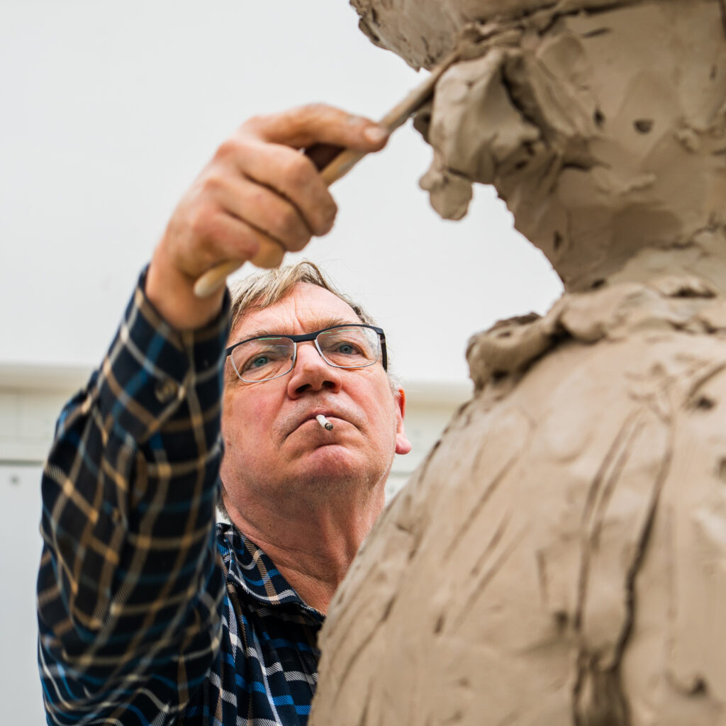 Ein Mann formt in Flanellhemd und Brille eine große Tonstatue – eines der Highlights des „Kulturellen Sommers“.