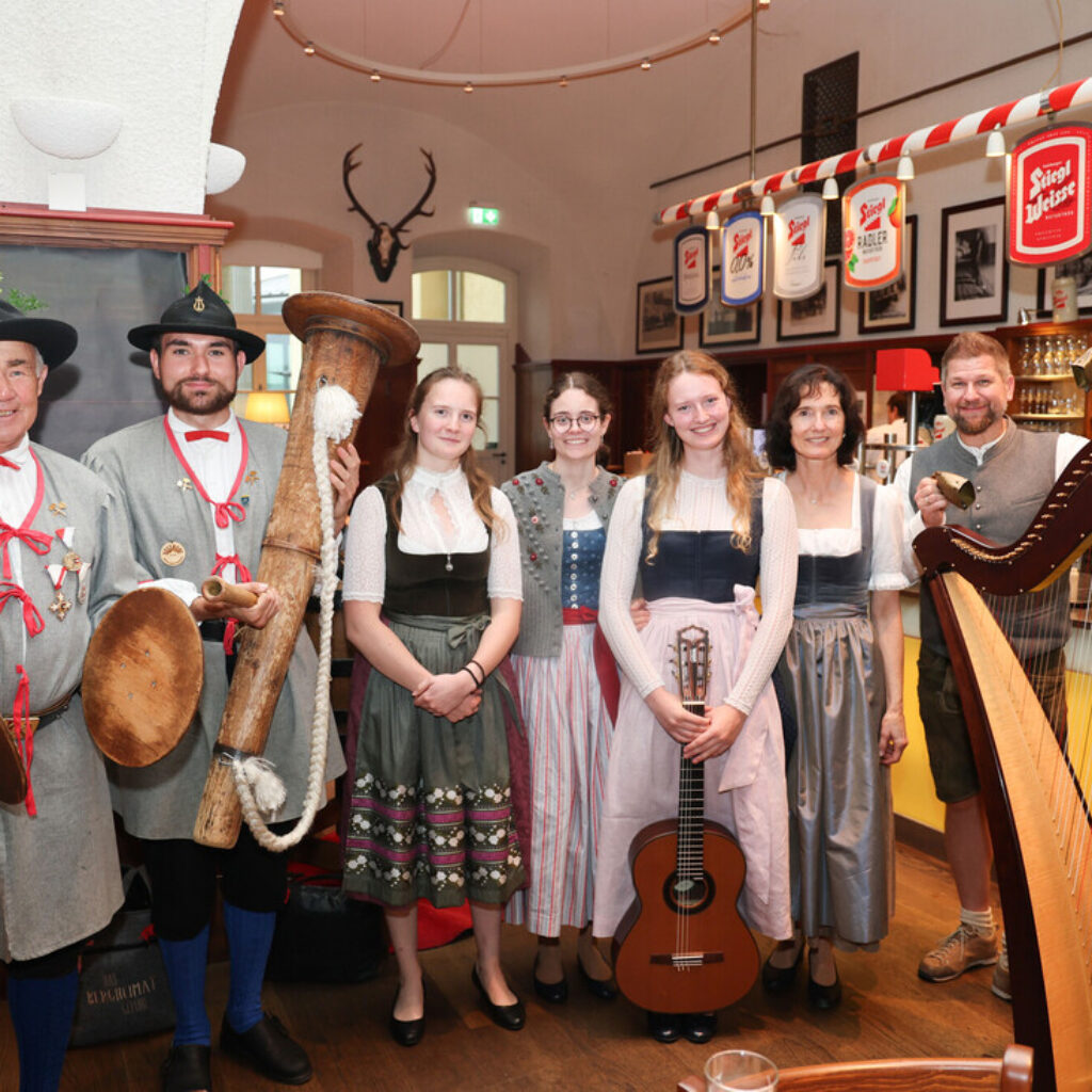 Eine Gruppe von Menschen in traditioneller österreichischer Tracht posiert mit Musikinstrumenten in einem gemütlichen, festlich geschmückten Raum.