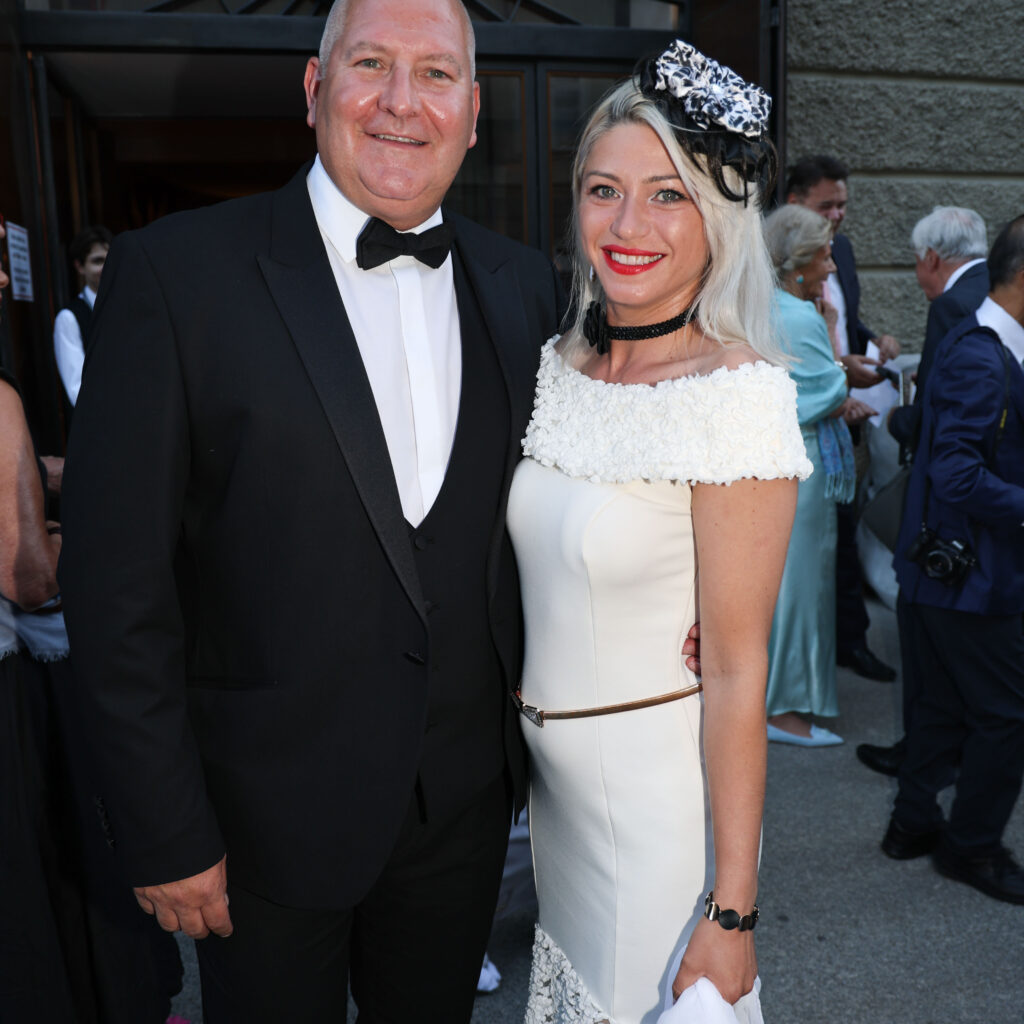 Ein Mann im Smoking und eine Frau in einem weißen Kleid posieren bei einer Feier im Freien anlässlich des UEFA-Supercups.