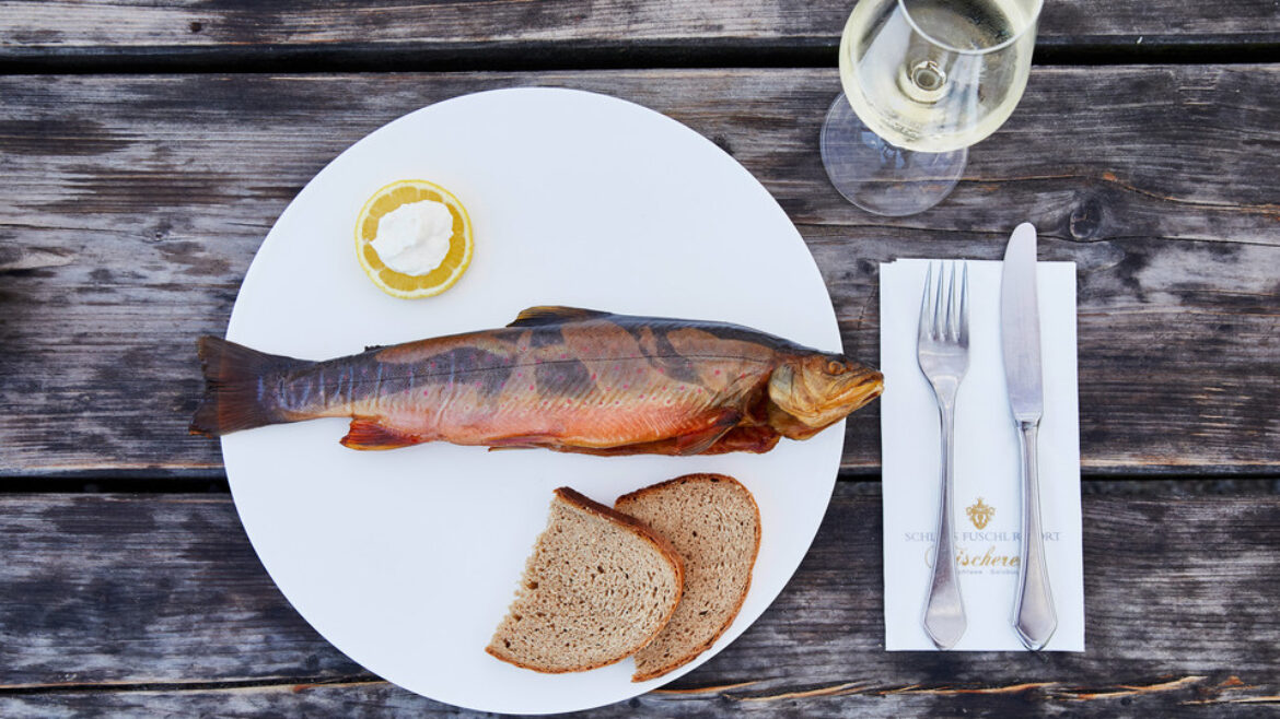 Ein ganzer geräucherter Fisch mit zwei Scheiben Brot, Zitrone und einem Glas Weißwein auf einem rustikalen Holztisch.