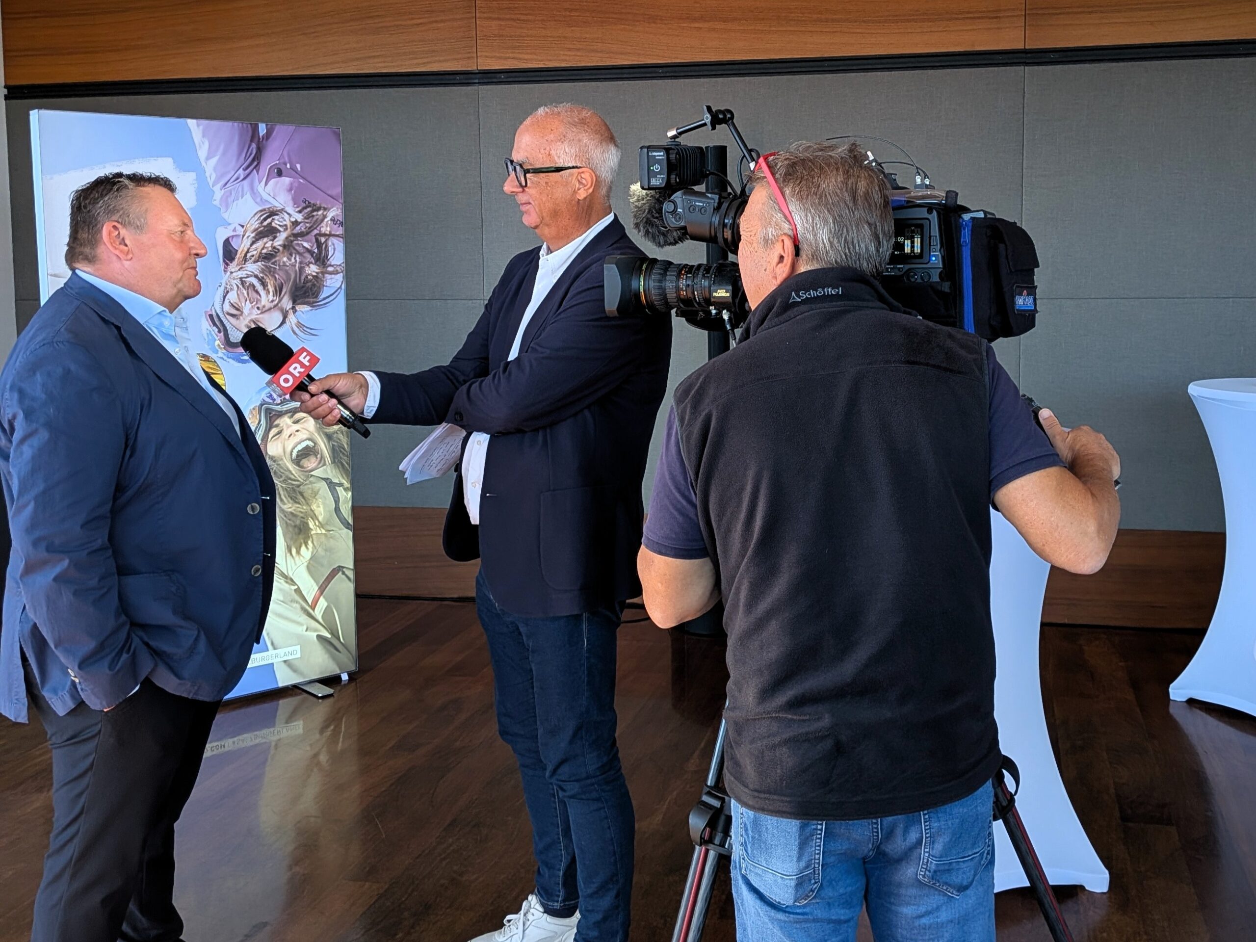 Ein Journalist interviewt einen Mann mit einem ORF-Mikrofon, während ein Kameramann die Szene filmt.