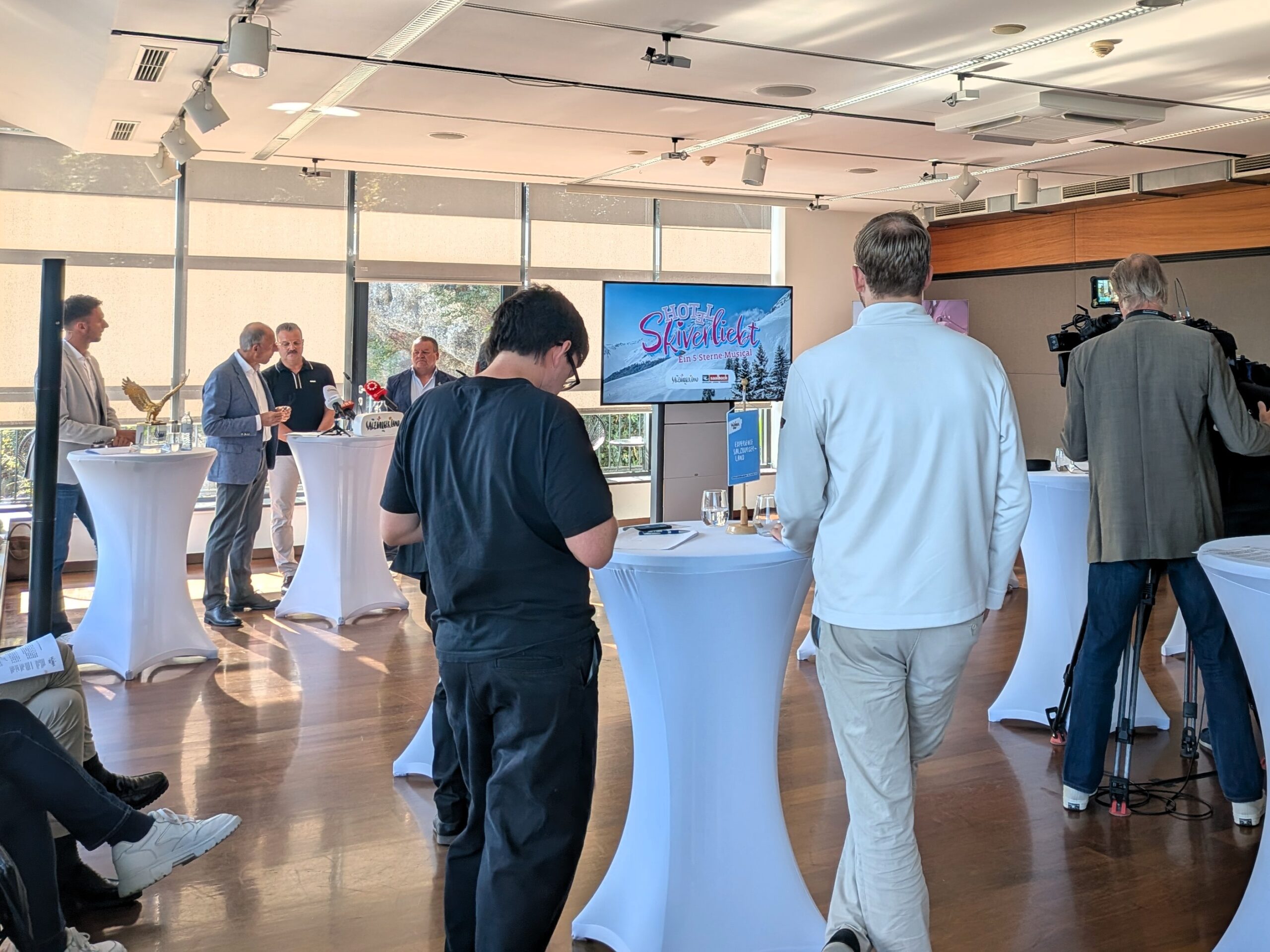 Die Menschen versammelten sich bei einer Pressekonferenz, bei der auf einem Bildschirm ein Musikwerbespot gezeigt wurde.