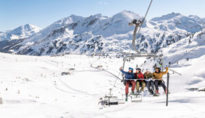 Vier Skifahrer sitzen auf einem Sessellift und machen ein Selfie vor der Kulisse der schneebedeckten österreichischen Berge.
