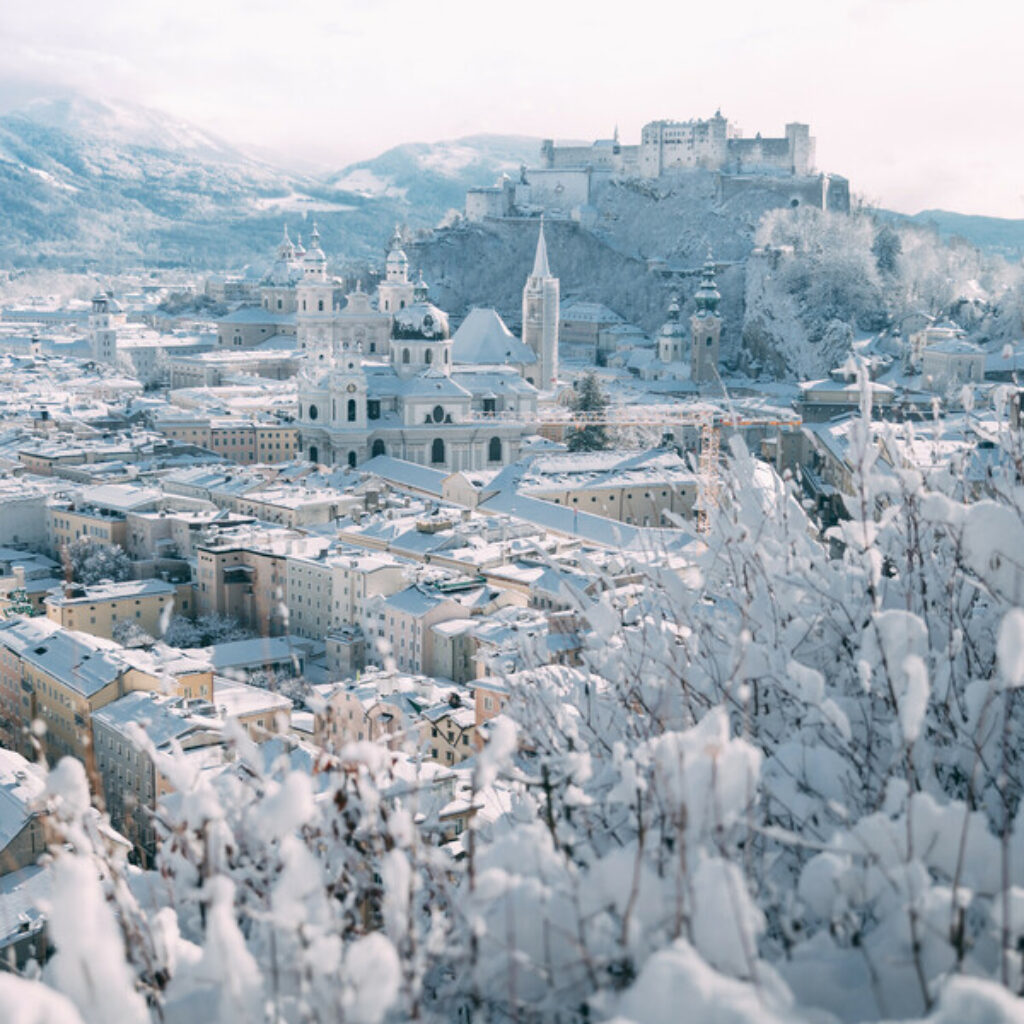 Ein verschneiter Blick auf die Skyline von Salzburg und die Festung Hohensalzburg unter einem winterlichen Himmel.