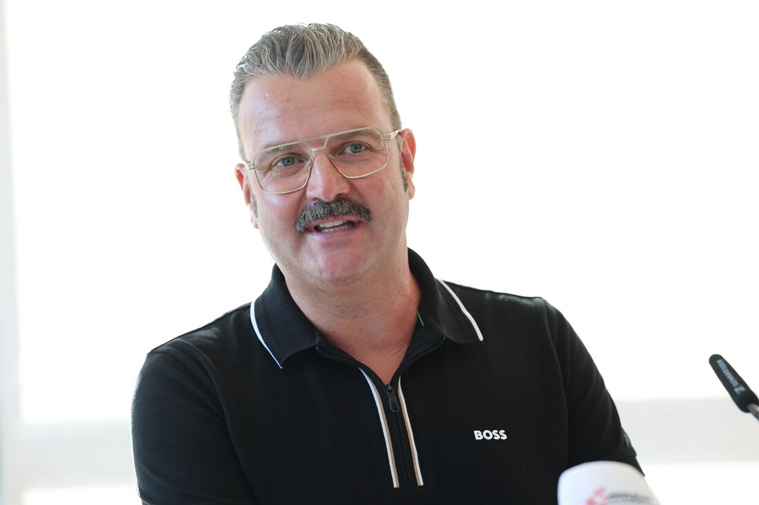 Ein Mann mit Schnurrbart und Brille, der ein schwarzes BOSS-Poloshirt trägt.