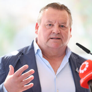 Ein Mann mittleren Alters in einem blauen Blazer, der in ein Mikrofon spricht.