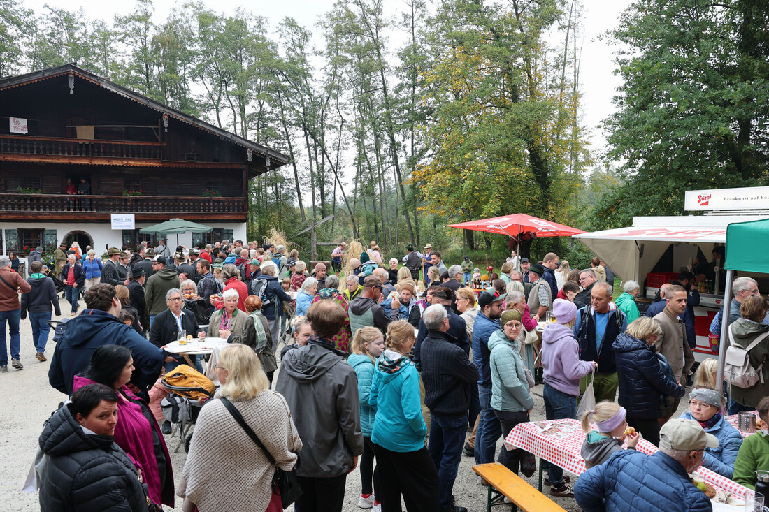 Bei einem Fest im österreichischen Stil mit Imbissständen und einem traditionellen Holzhaus versammelt sich draußen eine große Menschenmenge.
