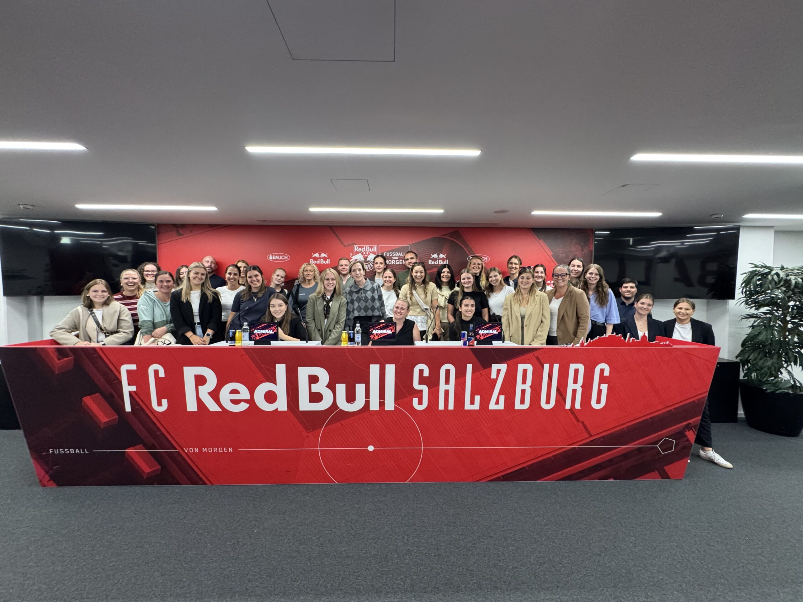 Eine große Gruppe von Menschen, die hinter einem roten Banner mit der Aufschrift FC Red Bull Salzburg für ein Foto posiert.