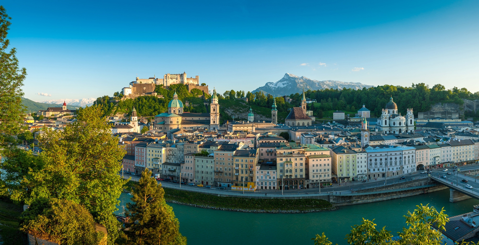 Panoramablick auf Salzburg, Österreich, mit bunten Gebäuden, einer Festung und Bergen im Hintergrund.