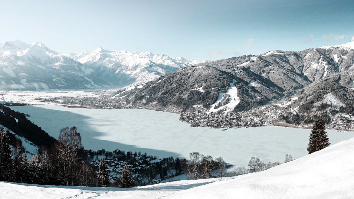 Schneebedeckte Berge und ein zugefrorener See unter klarem Himmel, mit einer kleinen Stadt am Ufer.