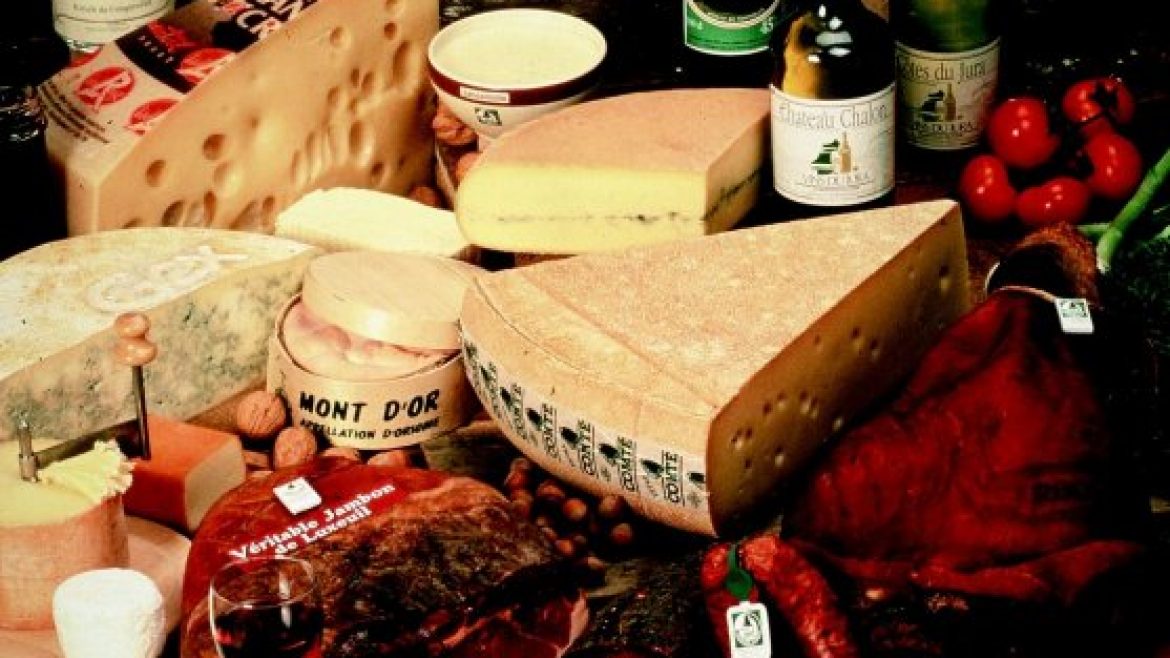 Verschiedene Käsesorten, Wurstwaren, Weinflaschen und frische Produkte werden auf einem rustikalen Tisch präsentiert.